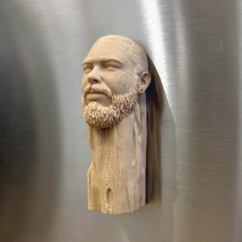 May include: A wooden sculpture of a man's head with a beard. The sculpture is carved in a realistic style and has a natural wood finish.