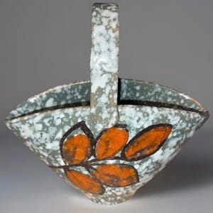 May include: A ceramic basket with a handle, featuring a speckled teal and white glaze. The basket is adorned with orange leaf designs outlined in black. The handle is white with a speckled pattern.