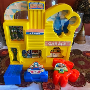 May include: A yellow plastic playset featuring Marvel Super Heroes Secret Wars. The playset has a garage, a building with a star-spangled banner, and a traffic light. There are three separate figures: Captain America, Spider-Man, and Doctor Doom.
