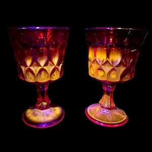 Könnte beinhalten: Zwei rubinrote Vintage-Becher mit rautenförmigen Mustern. Die Gläser haben einen kurzen Stiel und einen runden Fuß. Das Innere der Gläser hat einen gelben Farbton, und das Äußere hat einen violetten und roten Farbton.