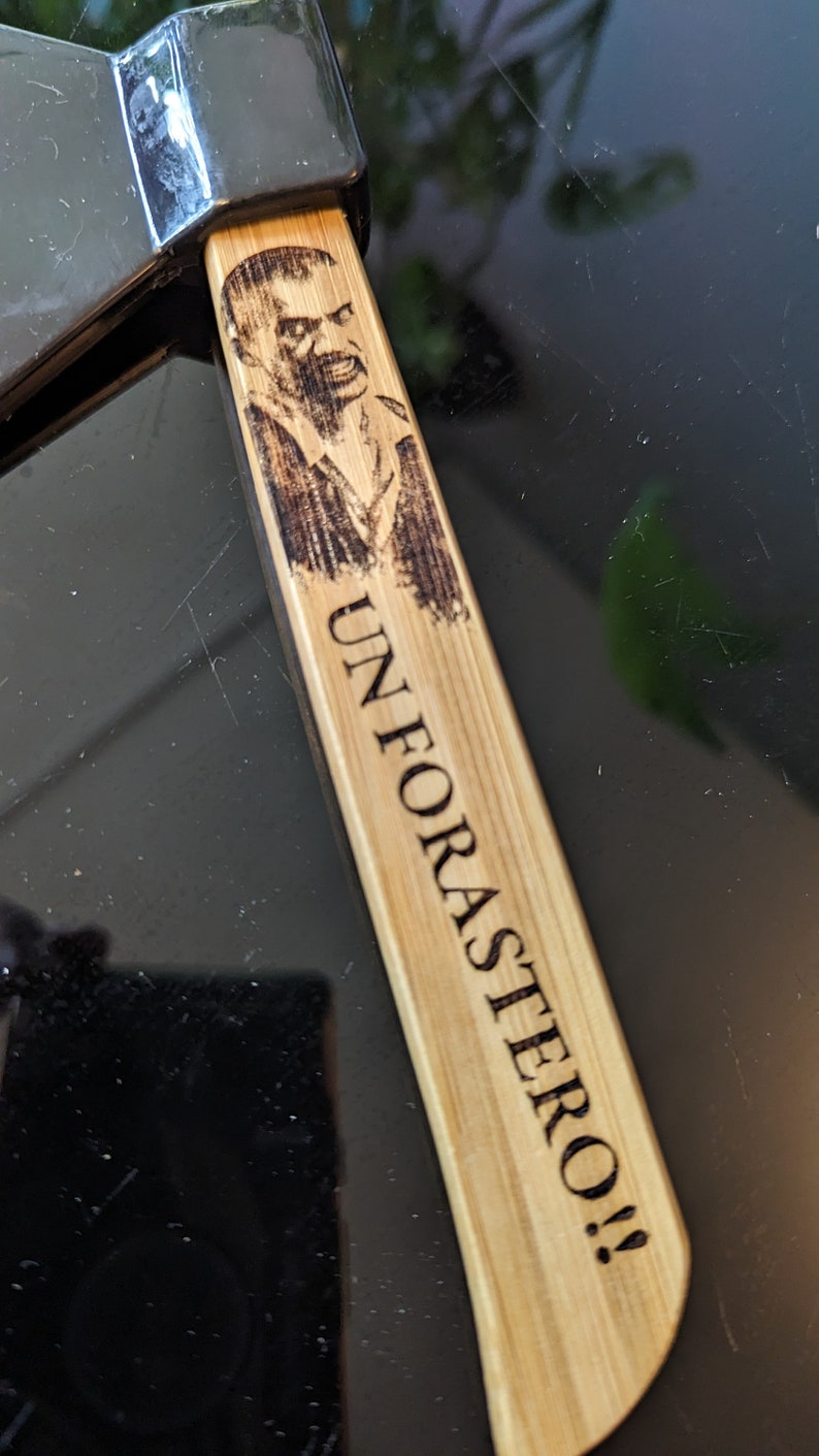 May include: A wooden axe handle with a burned-in image of a man's face and the text "UN FORASTERO!!"