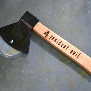 May include: A black pizza cutter shaped like an axe with a wooden handle. The handle is engraved with "4 resident evil".
