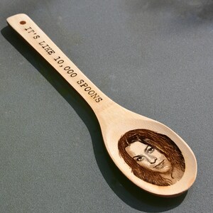 Puede incluir: Una cuchara de madera con el texto "It's like 10,000 spoons" grabado en el mango. Un rostro de mujer est&aacute; grabado en el cuenco de la cuchara.