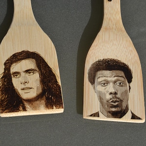 Puede incluir: Dos espátulas de cocina de madera con imágenes en blanco y negro de caras de hombres quemadas en la madera.