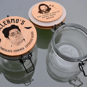 May include: Two glass jars with wooden lids. The lid on the left jar has a picture of a man with the text "Guillermo's Chocolate-Covered Espresso Beans". The lid on the right jar has a picture of a man with the text "Oh... You should really drink more water."