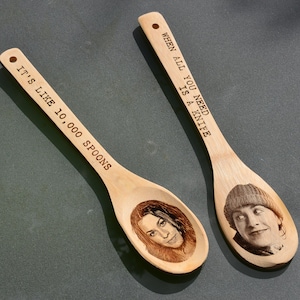 Puede incluir: Dos cucharas de madera con refranes grabados. Una cuchara dice "Cuando todo lo que necesitas es un cuchillo" y la otra dice "Es como 10.000 cucharas".