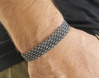 Könnte beinhalten: Ein geflochtenes Armband aus Silber mit einem gewebten Muster.