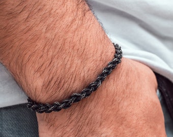 Könnte beinhalten: Ein schwarzes und graues Seil-Armband am Handgelenk einer Person.