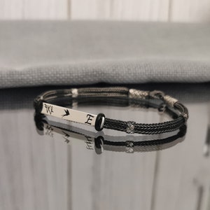 May include: A black braided bracelet with a silver charm featuring a bird and the letter "E".