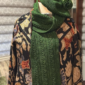 May include: A green knitted scarf and matching beret with a pom-pom. The scarf is draped over a black jacket with a floral pattern.