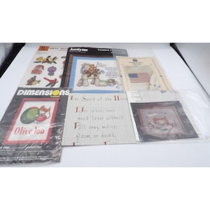 Puede incluir: Una colección de patrones de punto de cruz con varios diseños, que incluyen un ratón sosteniendo una aceituna, un caballo con un gato y un pájaro, una bandera y una casa con una cita sobre el espíritu de la casa. Los patrones están impresos en papel blanco con texto e imágenes negras.