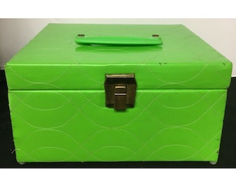 Puede incluir: Una caja de joyería acolchada de color verde brillante con un cierre dorado y una manija verde.