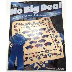 Puede incluir: Un libro titulado "No Big Deal" con el subtítulo "Dominando el arte del patchwork en miniatura". La portada presenta un edredón en miniatura con diseños en forma de abanico, bordes florales y una cinta azul.