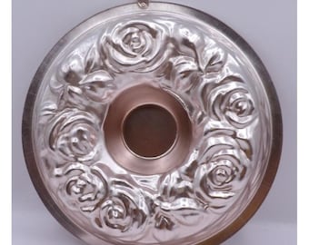 Puede incluir: Molde para pastel de metal plateado con un diseño de rosas. El molde tiene forma de anillo con un agujero en el centro.