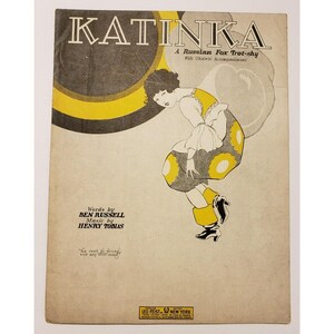 May include: A vintage sheet music cover for a song called "Katinka", a Russian Fox Trot-sky. The cover features a black and white illustration of a woman in a yellow and gray dress, dancing. The text "Words by Ben Russell, Music by Henry Tobias" is printed below the illustration.