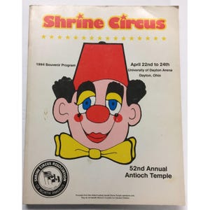 Puede incluir: Un programa de recuerdo del Shrine Circus de 1994. La portada presenta un payaso de dibujos animados con un fez rojo, una pajarita amarilla y el texto "Shrine Circus". El programa era para el 52º evento anual del Templo de Antioquía en Dayton, Ohio.