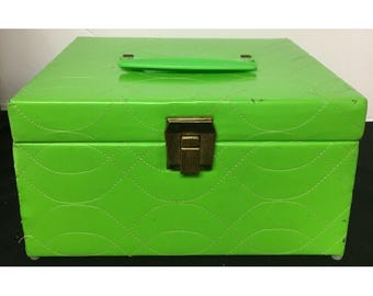 Puede incluir: Una caja de joyería verde brillante con un patrón acolchado y un cierre dorado. La caja tiene una manija de plástico.
