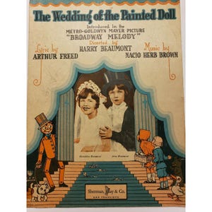 May include: Vintage sheet music cover for "The Wedding of the Painted Doll." The cover features the title in large, ornate lettering, with the names of the lyricist, director, and composer. A central image shows two children dressed as a bride and groom.