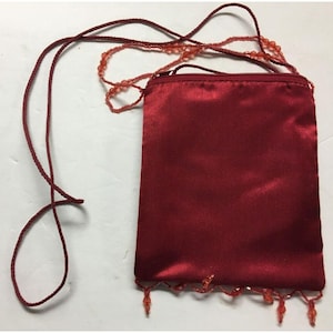 Puede incluir: Una pequeña bolsa de satén roja con una correa de cuentas. La bolsa tiene una cremallera y un fleco de cuentas.
