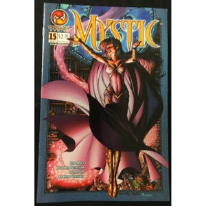 Może przedstawiać: Okładka komiksu Mystic #15, przedstawiająca kobietę w fioletowej i różowej sukni z falującą peleryną, trzymającą świecącą kulę. Okładka jest umieszczona na tle regałów z książkami.