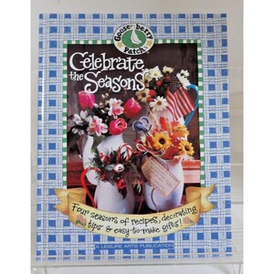 May include: A book titled "Celebrate the Seasons" by Gooseberry Patch. The cover features a blue and white checkered background with a floral arrangement in a white pitcher. The book is a Leisure Arts Publication.