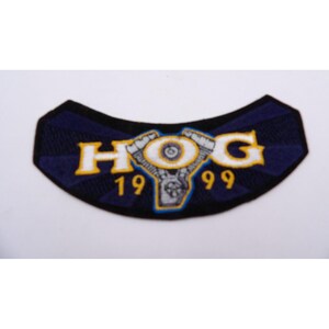 May include: A blue and yellow embroidered patch with the word "HOG" and the numbers "1999" around a stylized motorcycle engine.