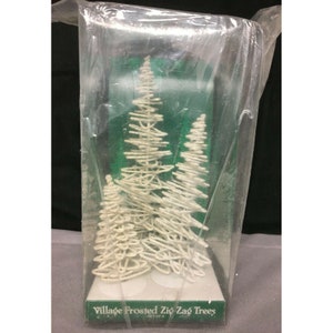 Può includere: Tre alberi bianchi a zig zag glassati in una confezione di plastica trasparente. La confezione ha uno sfondo verde con il testo "Village Frosted Zig Zag Trees".