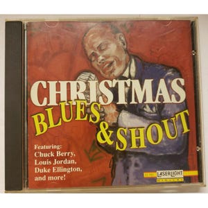 Puede incluir: Una caja de CD con un fondo rojo, blanco y azul. El texto "Christmas Blues & Shout" está en letras amarillas. La caja presenta una ilustración en blanco y negro de un hombre cantando en un micrófono. El texto "Featuring: Chuck Berry, Louis Jordan, Duke Ellington, and more!" está impreso en la caja.