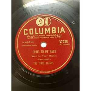 May include: Red vinyl record with a gold Columbia label. The record is titled "Cling to Me Baby" by Tiger Haynes and The Three Flames. The record number is 37935 (CO 38058).