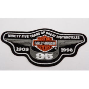 May include: A black and white Harley-Davidson patch with the text "NINETY FIVE YEARS OF GREAT MOTORCYCLES". The patch features the Harley-Davidson logo, the years 1903 and 1998, and the number 95.