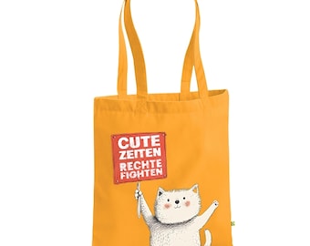 May include: A mustard yellow tote bag with a white cat illustration holding a sign that reads "CUTE ZEITEN RECHTE FIGHTEN" in red and white. The bag has matching yellow handles.