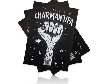 May include: A stack of black cards with white text and a white illustration of a fist with a star and plus signs. The text on the cards reads "CHARMANTIFA".