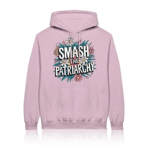 Könnte beinhalten: Ein hellrosa Kapuzenpullover mit einer zentralen Grafik aus bunten Blumen und grünen Blättern, die den fetten weißen Schriftzug SMASH THE PATRIARCHY umgeben, welcher in zwei Zeilen mit einem schwarzen Schlagschatten-Effekt angeordnet ist.