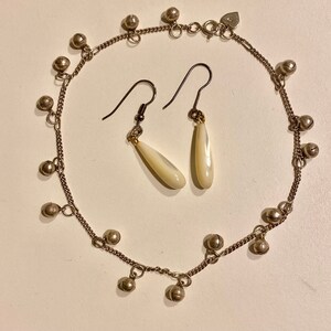 May include: A silver anklet with small bells and a pair of white teardrop earrings with silver hooks.