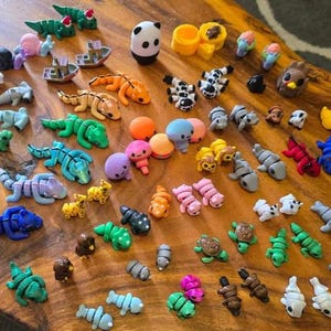May include: A collection of colorful, small, plastic animal figurines. The figurines are arranged on a wooden surface and include a variety of animals, such as a panda, a turtle, a fish, a bird, and a frog.