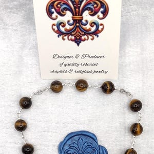 Peut inclure: Un chapelet fait à la main avec des perles en œil de tigre, un crucifix en argent et une médaille de Saint Christophe. L'image comprend un sceau de cire bleu avec une fleur de lys et une carte "Rosaries by Marcie".
