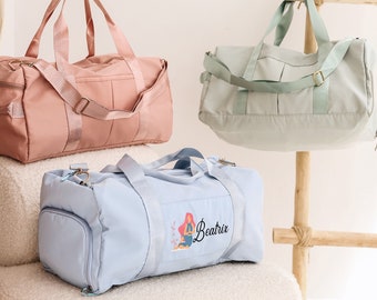 May include: Three duffel bags in pastel colors: pink, mint green, and light blue. The light blue bag has a graphic of a person in a yoga pose with the name "Beatrix". Each bag has a shoulder strap and handles.