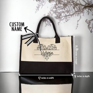 May include: A black and white canvas tote bag with a black handle. The bag features a white heart design with a mandala pattern and the name "Victoria" written in black. The bag measures 17 inches wide, 11.81 inches high, and 9 inches deep.