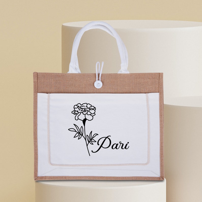 May include: A white tote bag with brown burlap accents. The bag has a white pocket with a black floral design and the word "Pari" written in cursive.