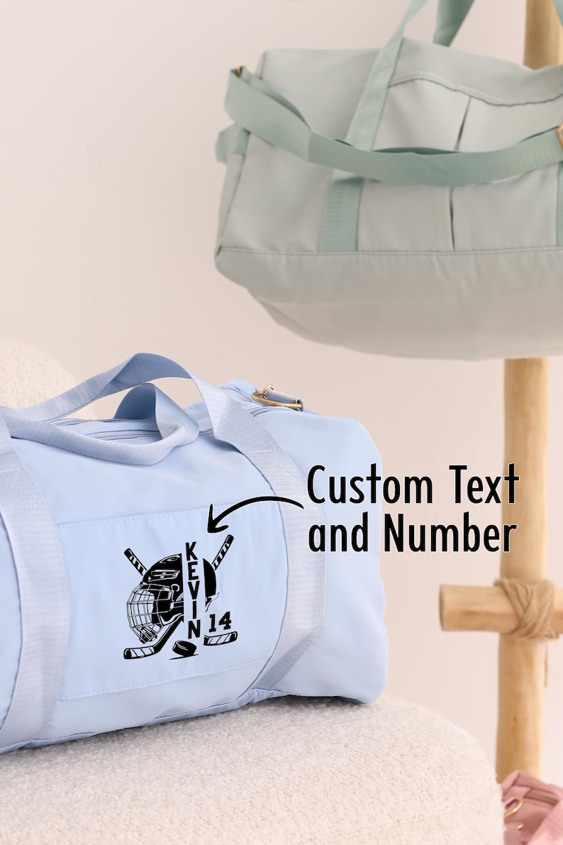 May include: Light blue duffel bag with a hockey helmet and sticks graphic and the text "KEVIN 14" embroidered on the front. Custom Text and Number.