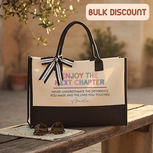 May include: A canvas tote bag with black handles and a black and white striped bow. The bag has a cream-colored upper section and a dark brown bottom. Text on the bag reads "ENJOY THE NEXT CHAPTER" and "NEVER UNDERESTIMATE THE DIFFERENCE YOU MADE".