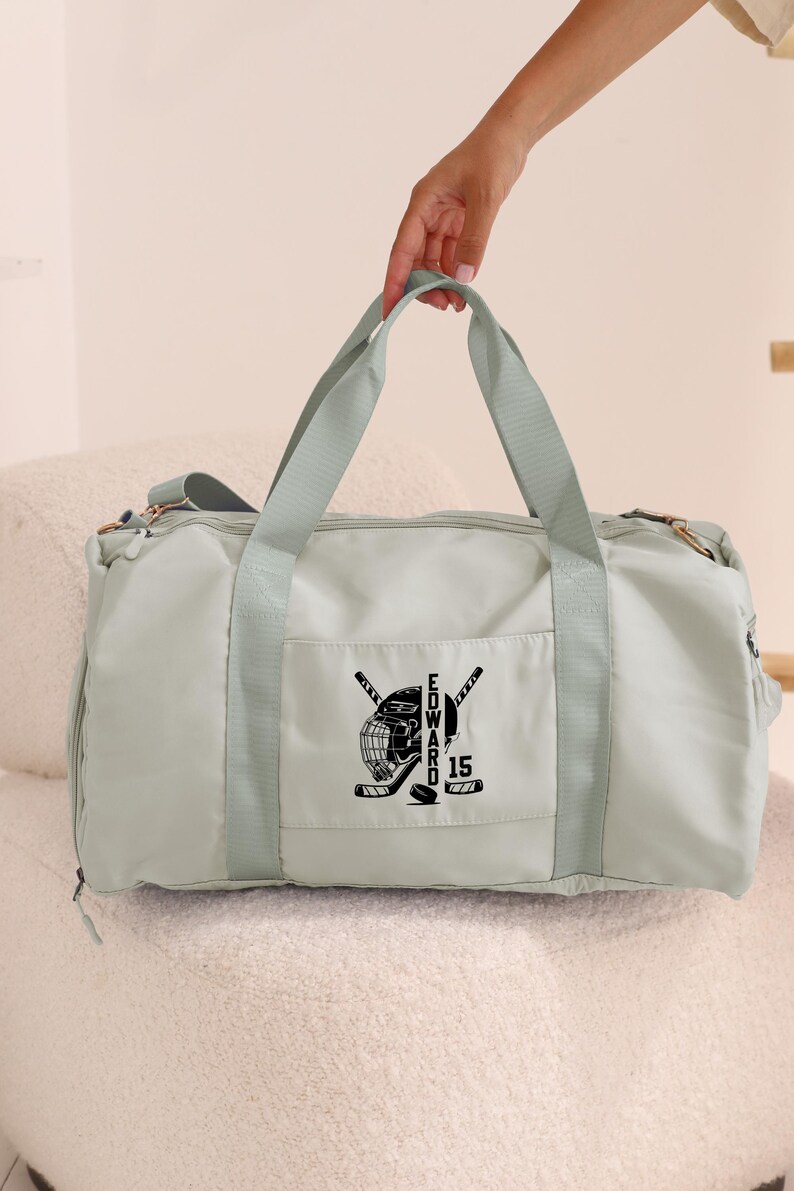 May include: A light green duffel bag with a black hockey helmet and crossed hockey sticks design. The text "EDWARD" and the number "15" are also embroidered on the bag.