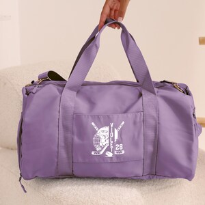 May include: Purple duffel bag with a white hockey helmet and stick graphic, the text "VIOLET 28" is printed on the bag.