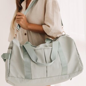 May include: A light blue duffel bag with a long adjustable strap. The bag has two top handles and a zipper closure.