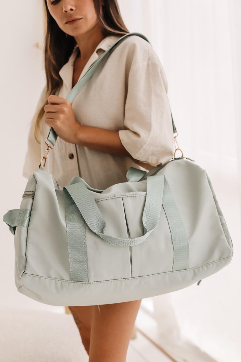 May include: A light blue duffel bag with a long adjustable strap. The bag has two top handles and a zipper closure.