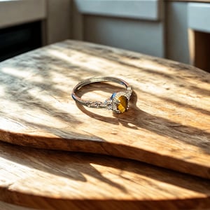 May include: A silver ring featuring a large oval-shaped gemstone set in an ornate silver setting. The gemstone is a light brown colour with a golden sheen.