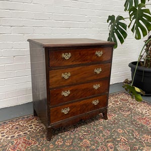 May include: A four-drawer chest in dark wood, featuring brass handles. The chest has a rectangular shape with a gently curved base and rests on short legs. The wood grain is prominent, suggesting an antique piece, likely around 90 cm in height.