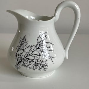 Peut inclure: Crémier en céramique blanche avec un motif de branches d'arbre noir. Le crémier a une poignée incurvée et un bec verseur. Le design est un ajout minimaliste et élégant à toute table.