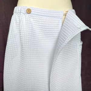 Può includere: Accappatoio bianco in spugna a nido d'ape con un bottone in legno e una chiusura a nodo.