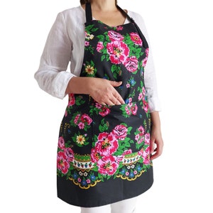 May include: Black apron with a floral print featuring pink, red, green, and yellow flowers. The apron has a large pocket on the front and adjustable straps.